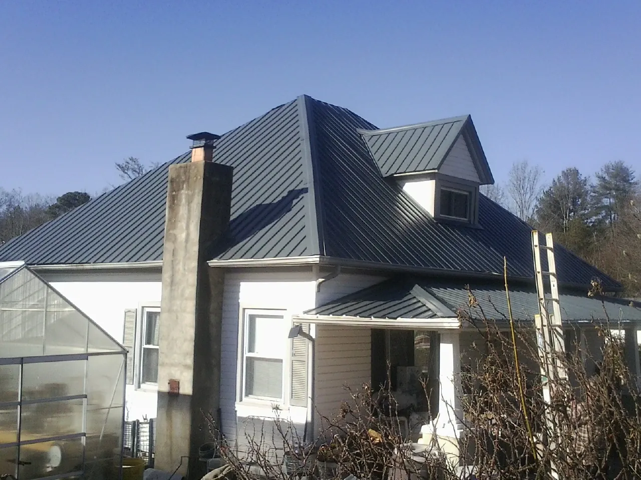 Dark blue standing seam metal roof on a white farmhouse with dormer — Slate & Tile Roof Repair by Roofing Brothers in Delevan