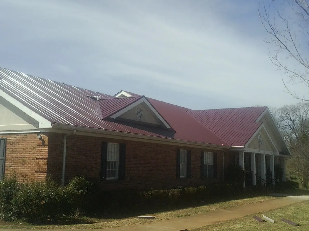 Red metal roof with gabled entries on a long brick building, from a Hail Damage Roof Repair job in Delevan