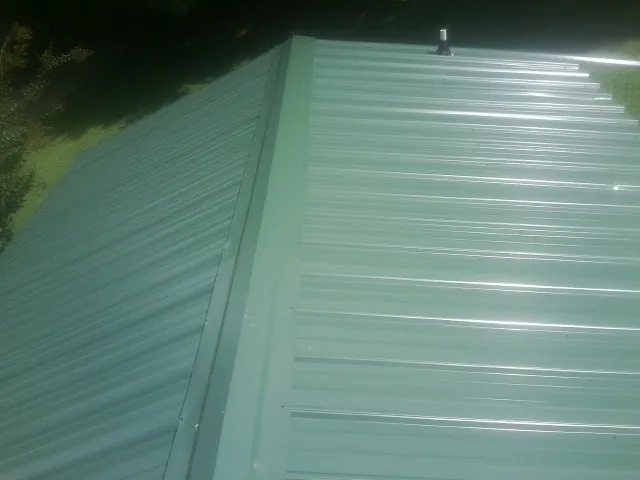 New green metal panels meeting at the ridge of a roof — Flat Roof Repair work by our crew in Delevan