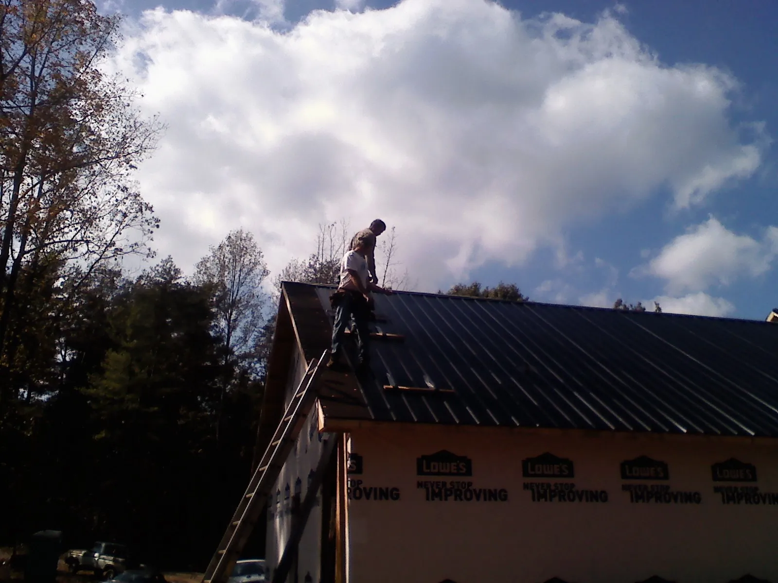 Roofer fastening dark metal panels high against a cloudy sky, from a Roof Inspection job in Delevan