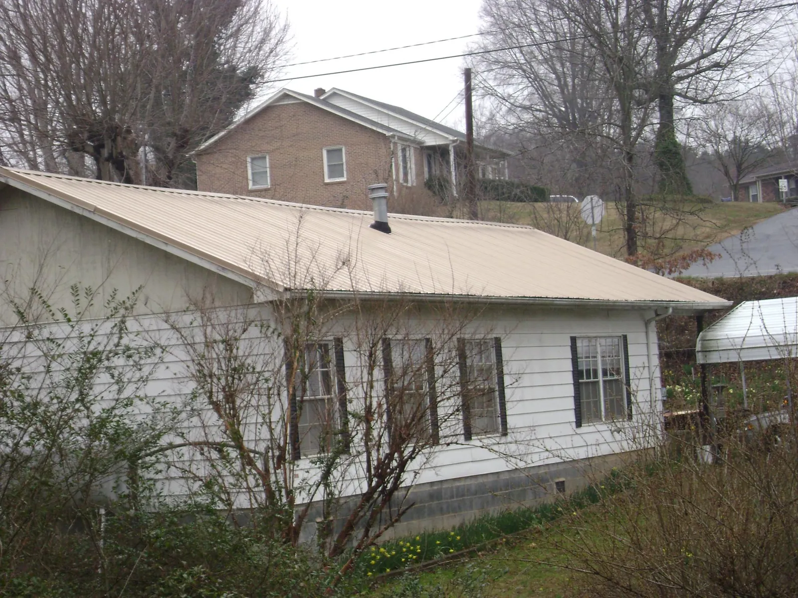 Tan metal roof on a white sided house set into a hillside — Commercial Roofing by Roofing Brothers in Delevan