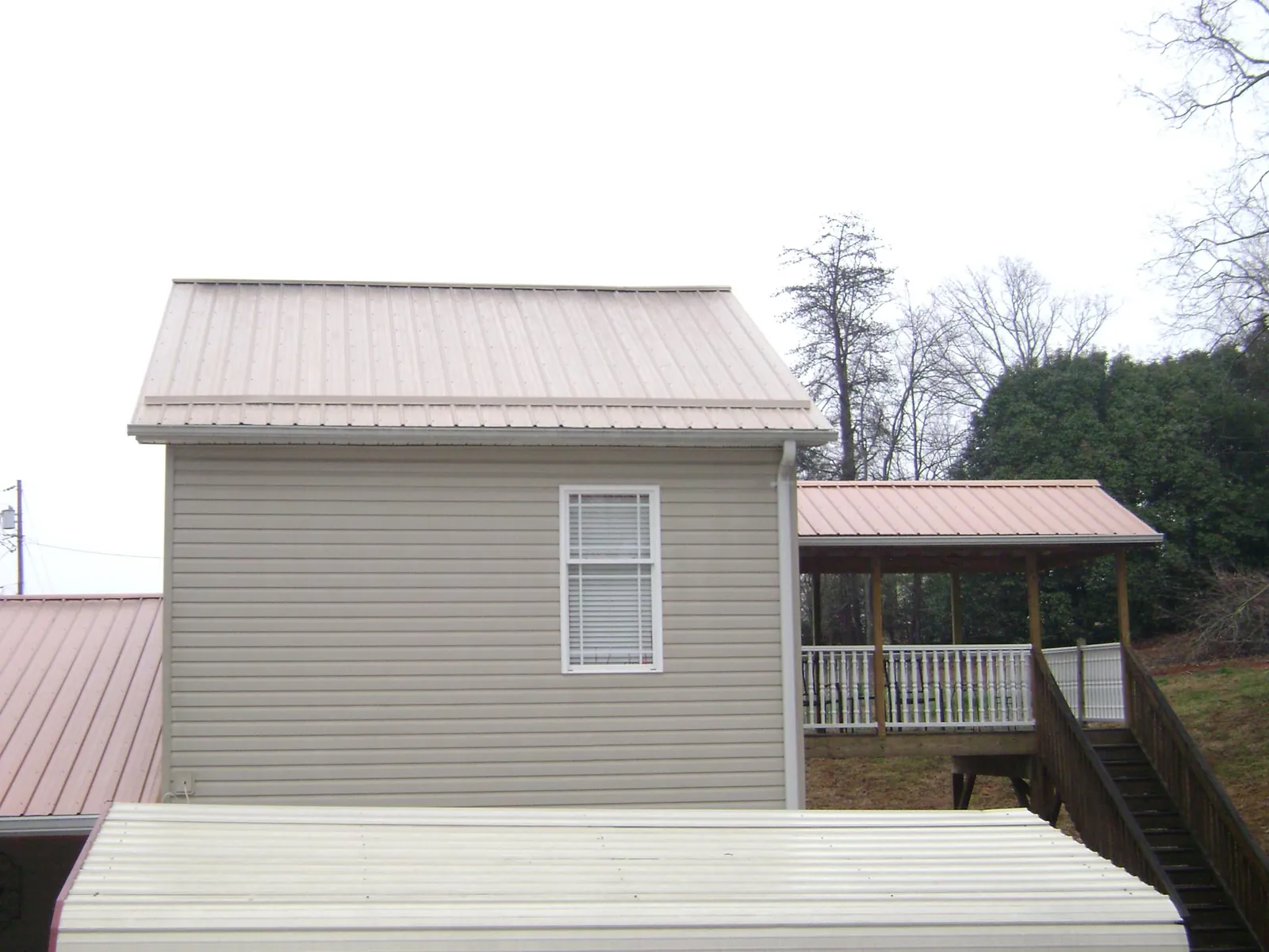 Tan metal roofs on a two story addition and attached porch, from a Roof Replacement job in Delevan