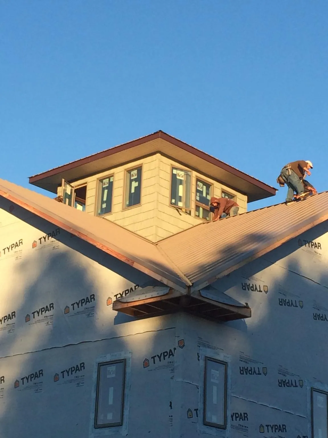 Roofers working around a rooftop cupola on a new metal roof at sunset — Roof Waterproofing in Delevan by Roofing Brothers
